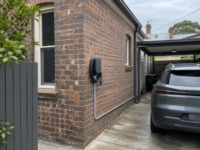 EV charger mounted on a brick exterior wall beside a driveway and parked car in Dulwich Hill