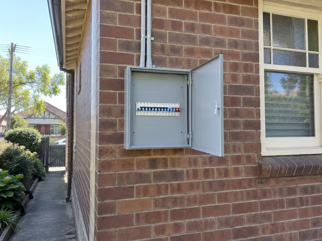 Open external switchboard on a brick house wall beside a window in Croydon